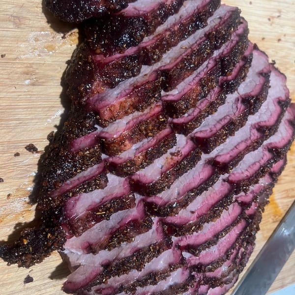 Thinly sliced, smoked brisket with a dark, peppery crust on a wooden cutting board.