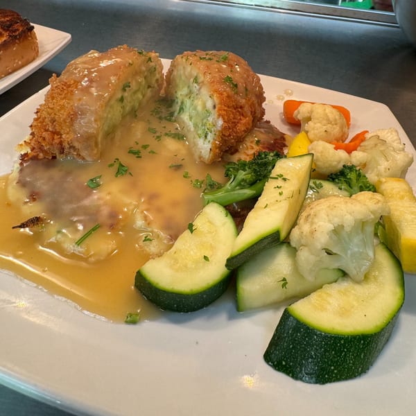 Chicken Kiev with gravy, mashed potatoes, and steamed vegetables on a white plate.