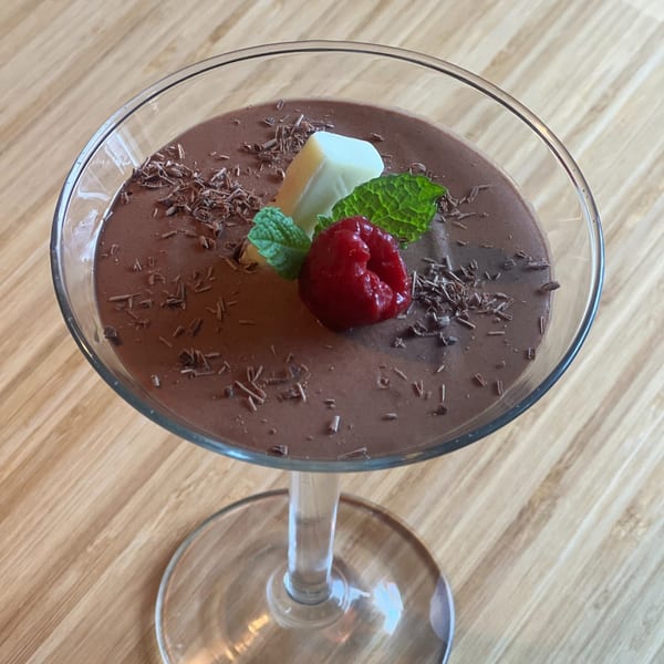 Chocolate mousse in a martini glass, garnished with a raspberry, mint leaves, and chocolate shavings.
