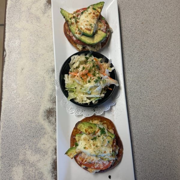 Two avocado and melted cheese toasts with a side of coleslaw on a white rectangular plate.