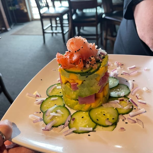 A colorful tuna poke tower with avocado, mango, and pickled ginger, garnished with cucumber and onion.