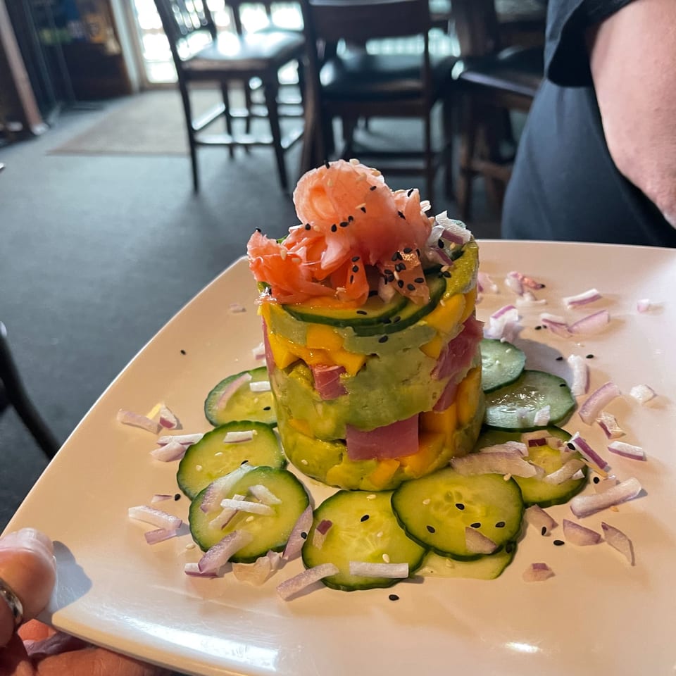A colorful tuna poke tower with avocado, mango, and pickled ginger, garnished with cucumber and onion.